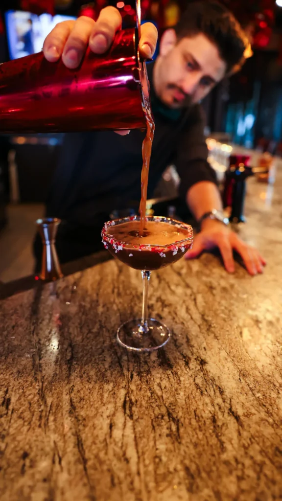 Bartender pouring a holiday cocktail into a candy-cane-rimmed coupe