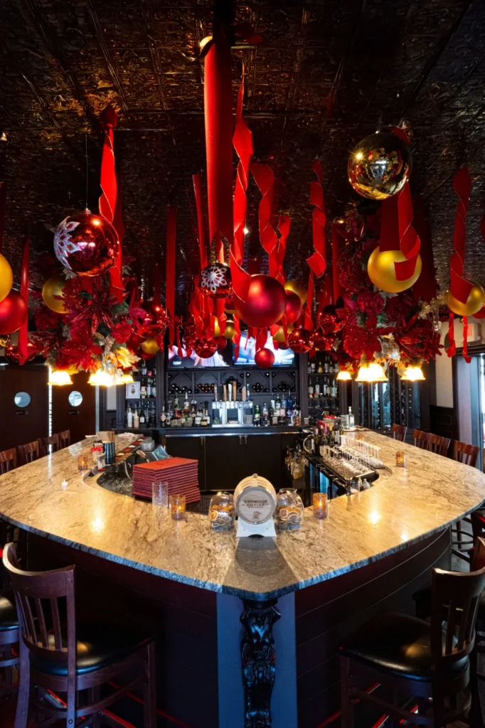 Bar ceiling hung with red ribbons and oversized red and gold ornaments for A Sinner's Christmas Experience