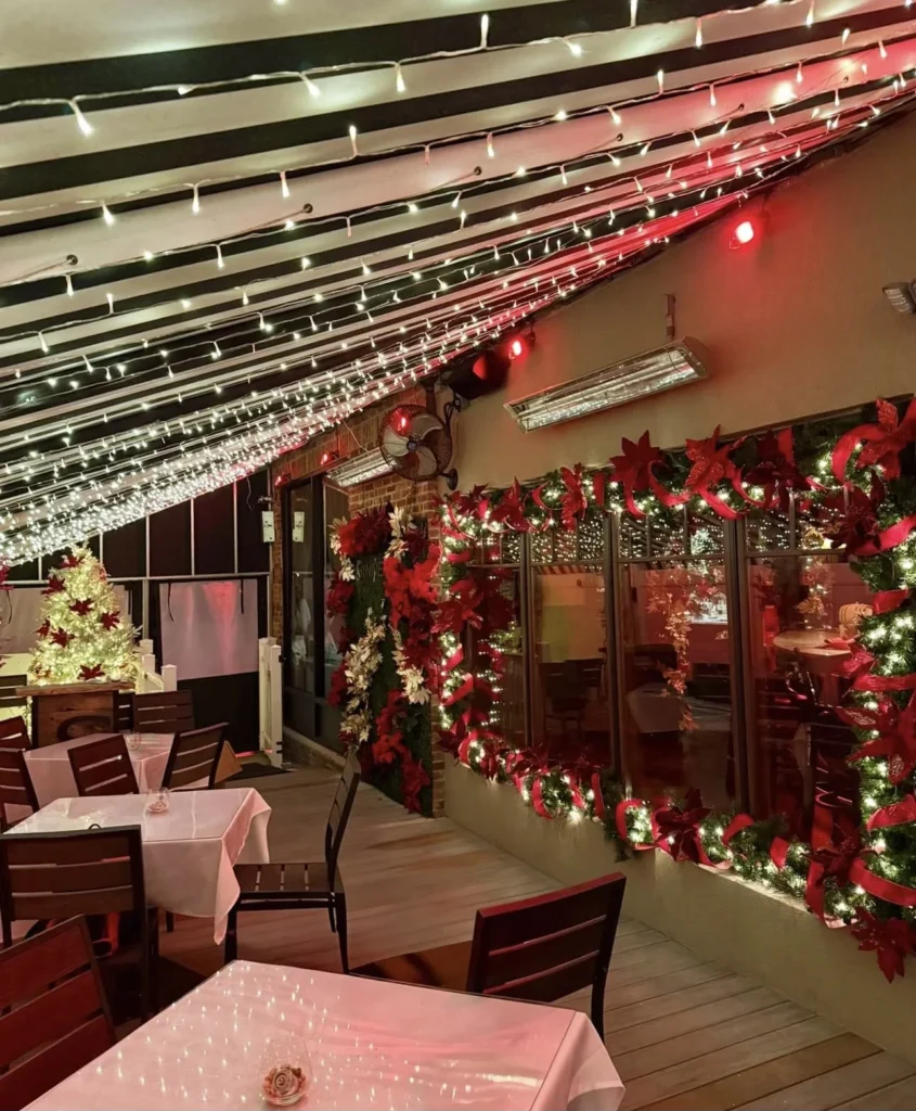 Patio under string lights with garland-framed windows and a lit Christmas tree